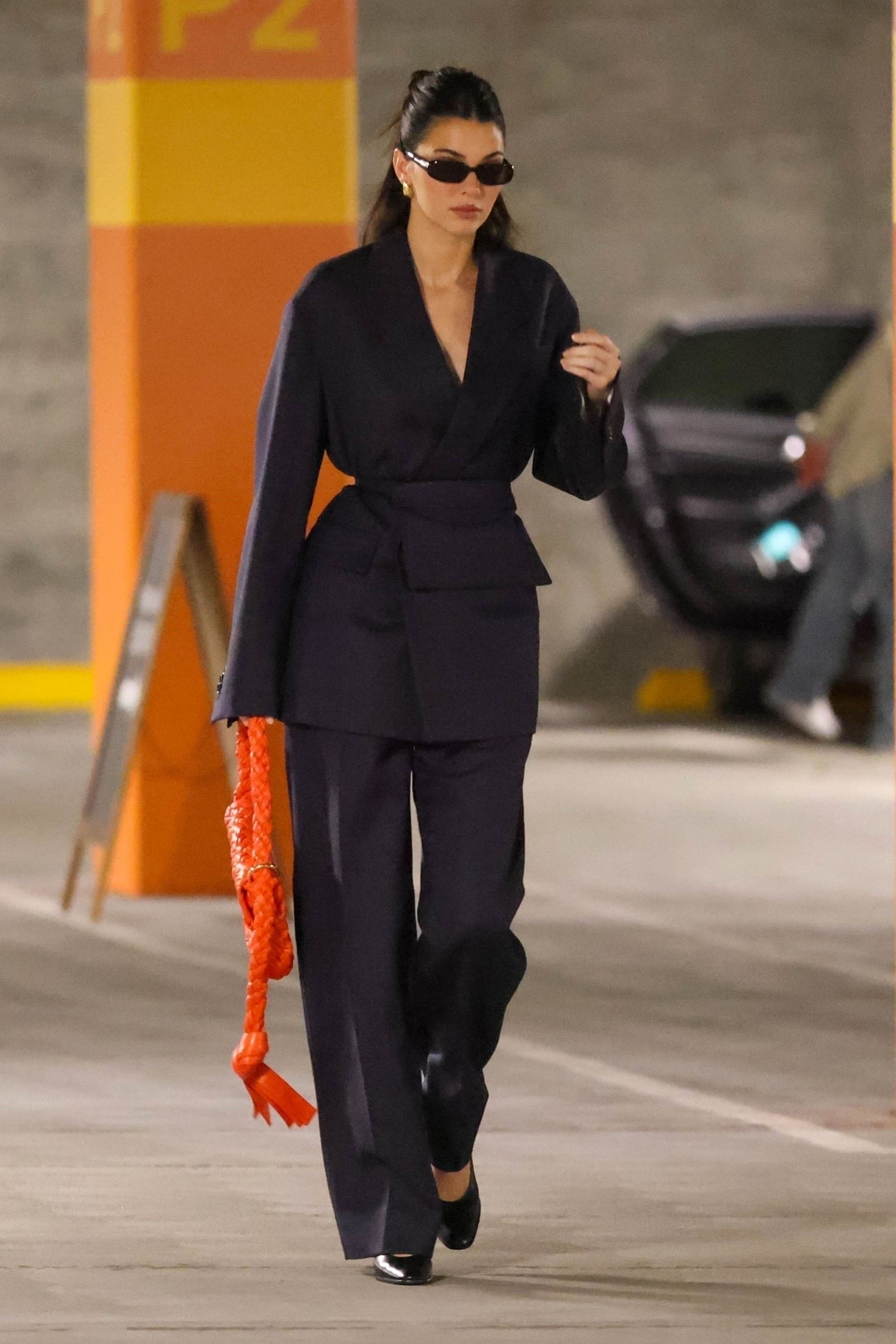 Kendall Jenner wears a suit with an orange bag and sunglasses.