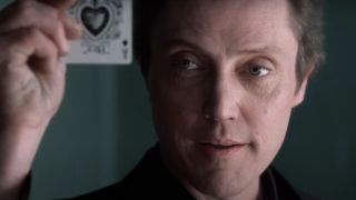 Christopher Walken holding up an Ace playing card and smirking in King of New York