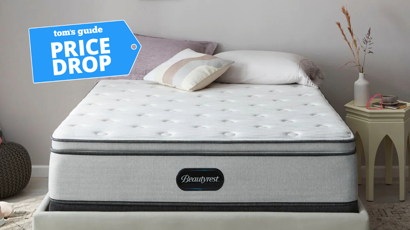 A white and black mattress in a brightly lit room with pillows on top and a side table next to it