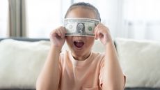 A young girl holds a dollar bill over her eyes.