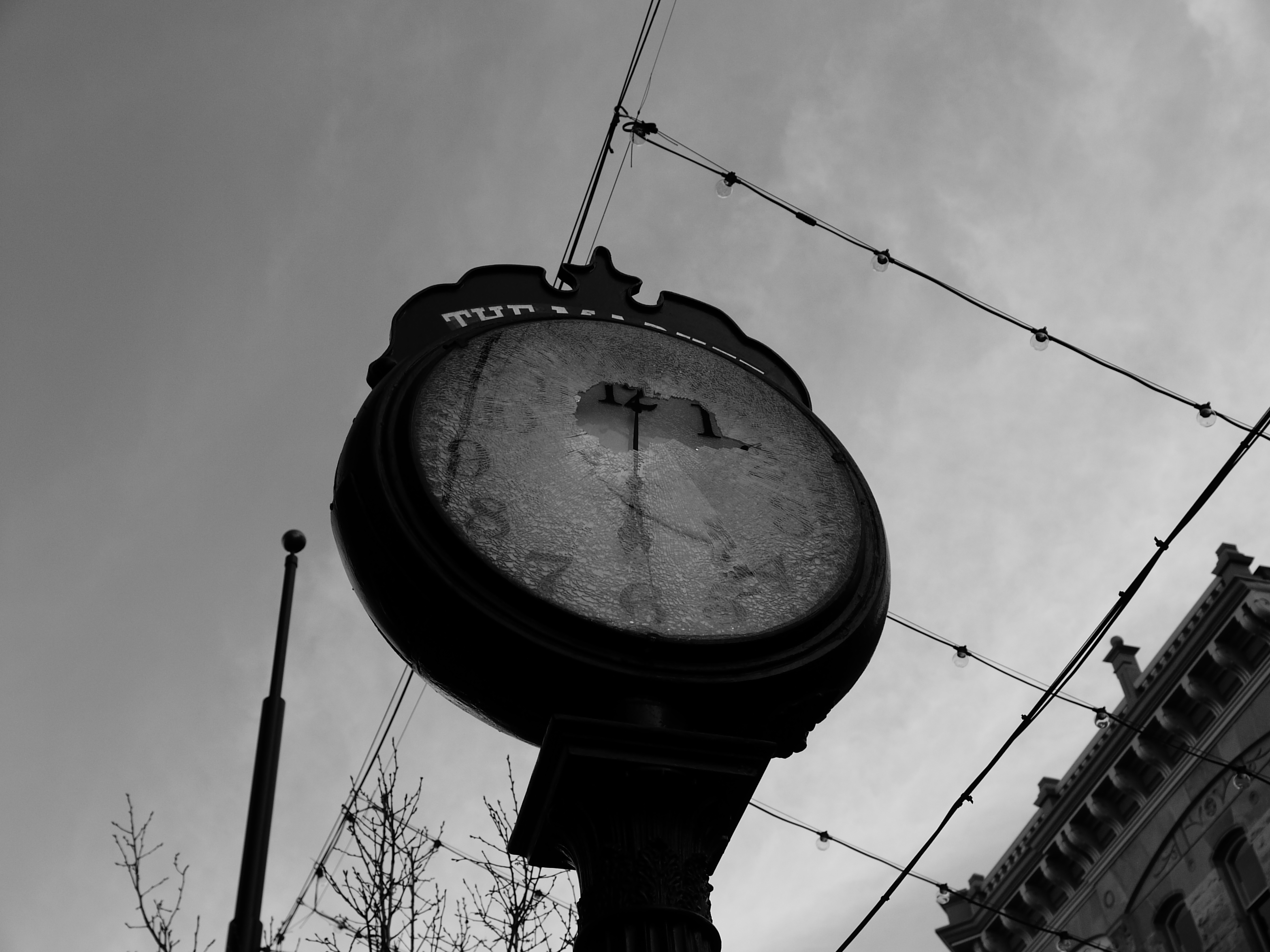 A black and white photo of a large clock with a broken glass face, shot on the Lumix L1