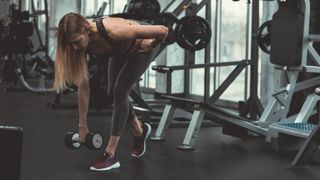 Woman performs split-stance Romanian deadlift with dumbbell in gym