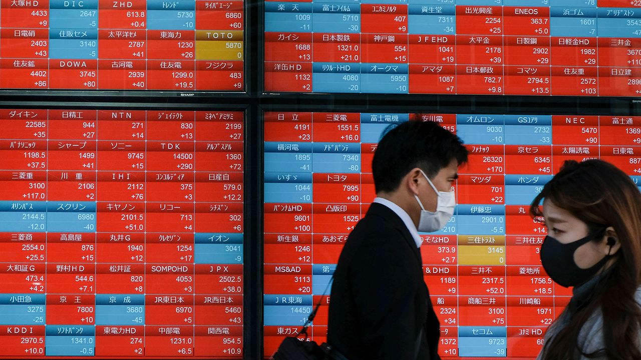 People walk past a board displaying Nikkei 225 stock prices