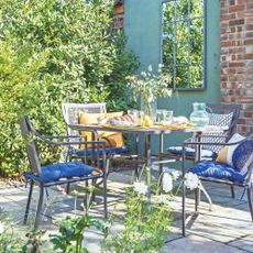 Garden mirror on blue wall next to outdoor seating area with blue cushions