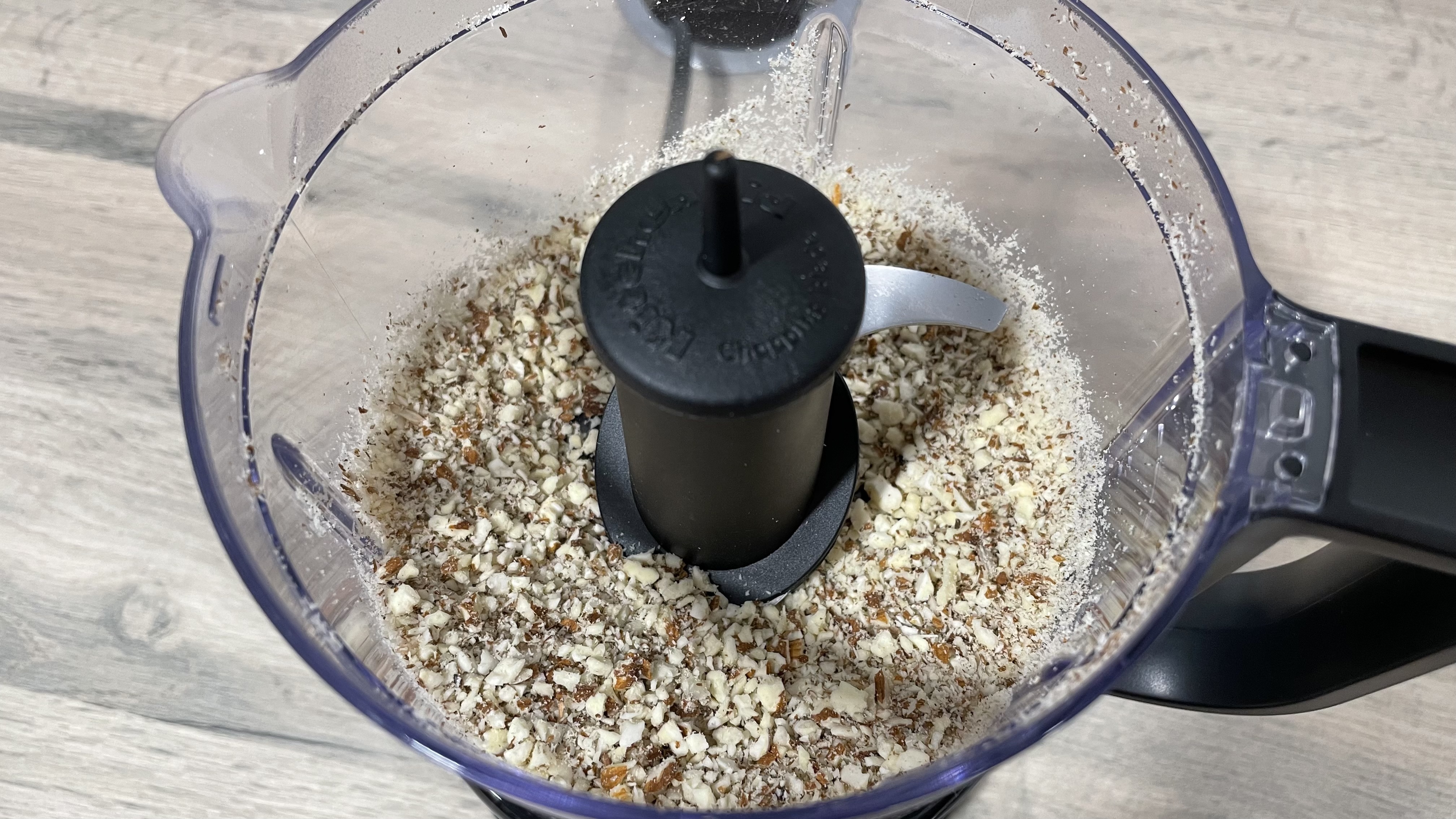 A close up view of chopped almonds inside the work bowl of the KitchenAid Mini Food Chopper.