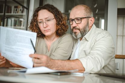 A mature couple reviews paperwork while sitting at their dining table.