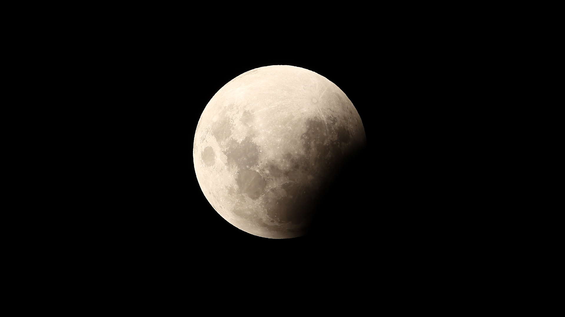 A full moon is photographed in a black sky with the lower right edge obscured by the Earth's shadow during an eclipse. Dark spots called lunar maria mark the surface, where lava once flooded ancient impact craters.