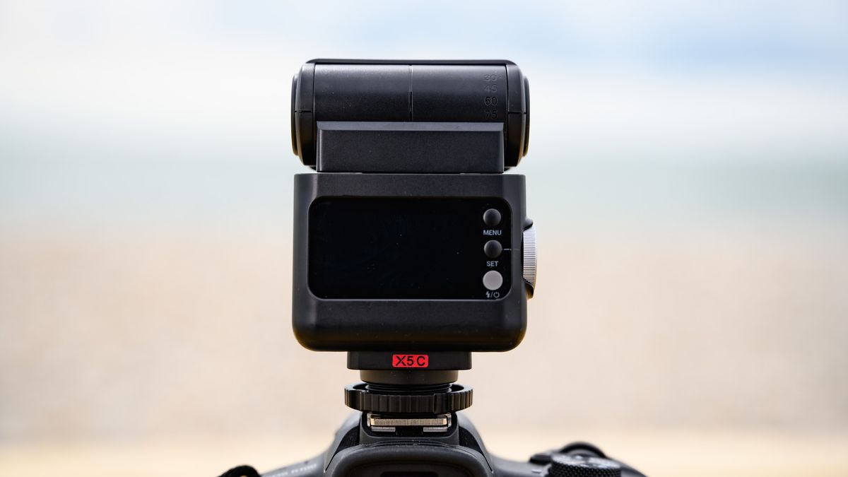 Closeup of the Godox iT32 camera flash and its rear display, the ocean is behind it