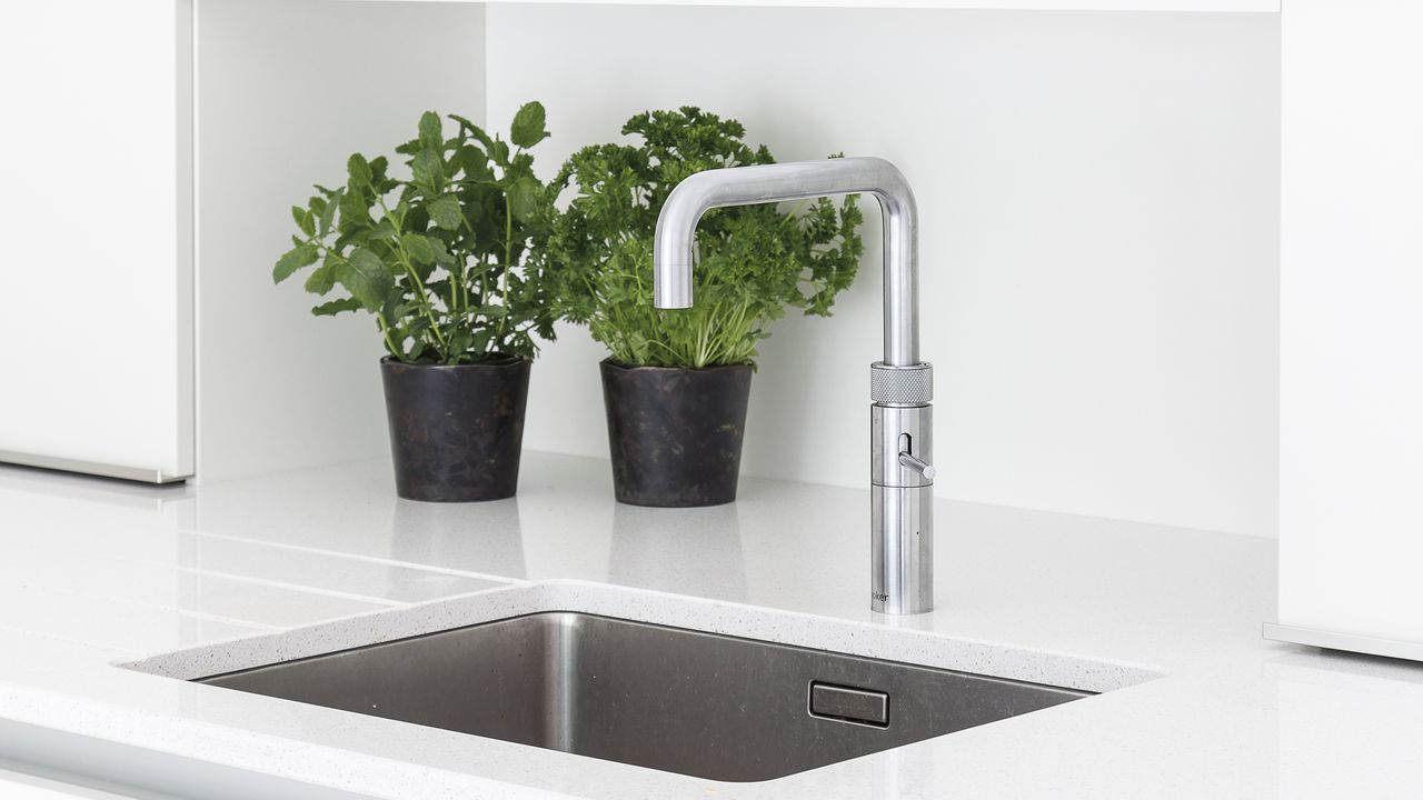 metal boiling water tap over grey sink in white kitchen counter next to white cabinets, with potted herbs 