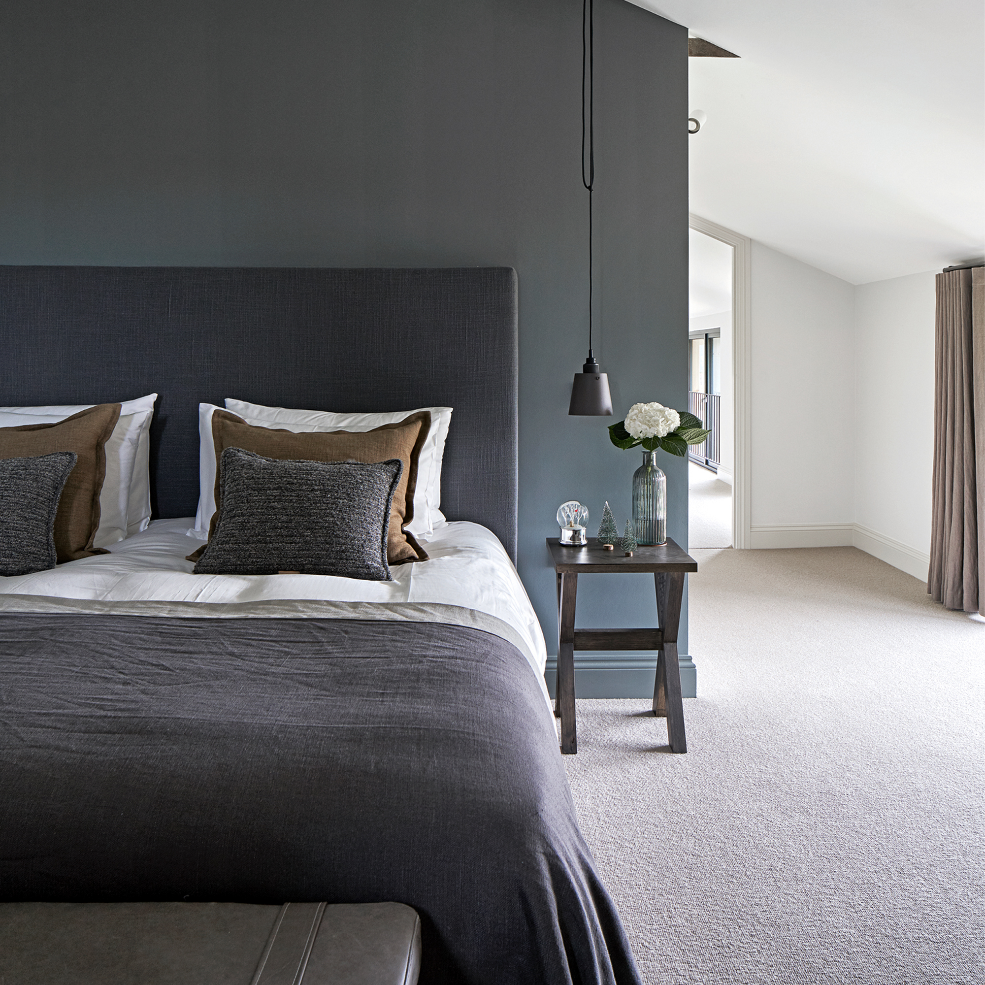 A blue bedroom with a bed dressed in white, grey, and brown bedding