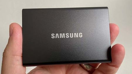 Close-up of a hand holding a sleek, black Samsung external hard drive against a plain background. The device is compact and rectangular with a matte finish.