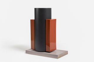 A futuristically designed, minimalist sculpture in black and orange tones sits in a white gallery.