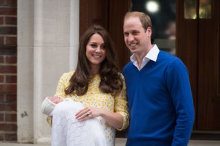 Princess Kate wears a yellow floral dress and holds a baby Princess Charlotte outside the Lindo Wing, while Prince William wears a white shirt and blue sweater