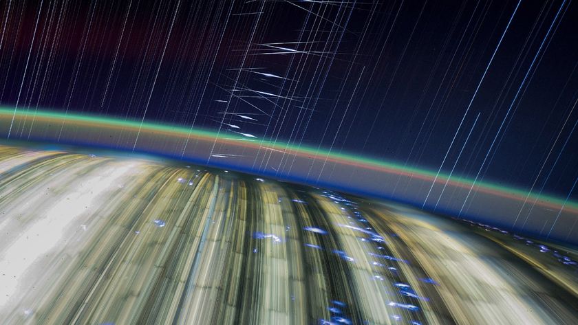 streaks of light crisscross a dark blue sky above a blurry earth below