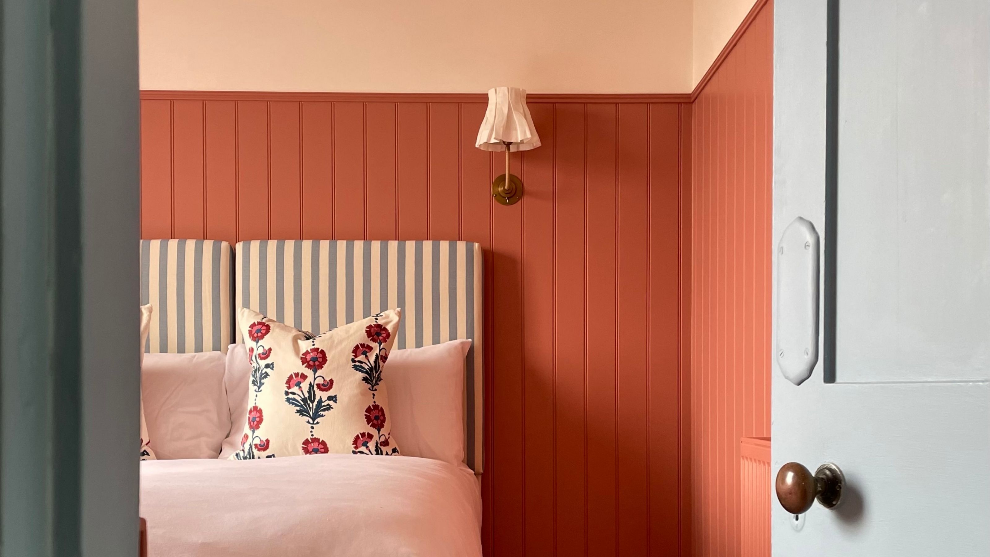 Image of a bedroom from a blue doorway that has salmon pink panelling going up three quarters of the wall, then there is a pink-toned white color.
