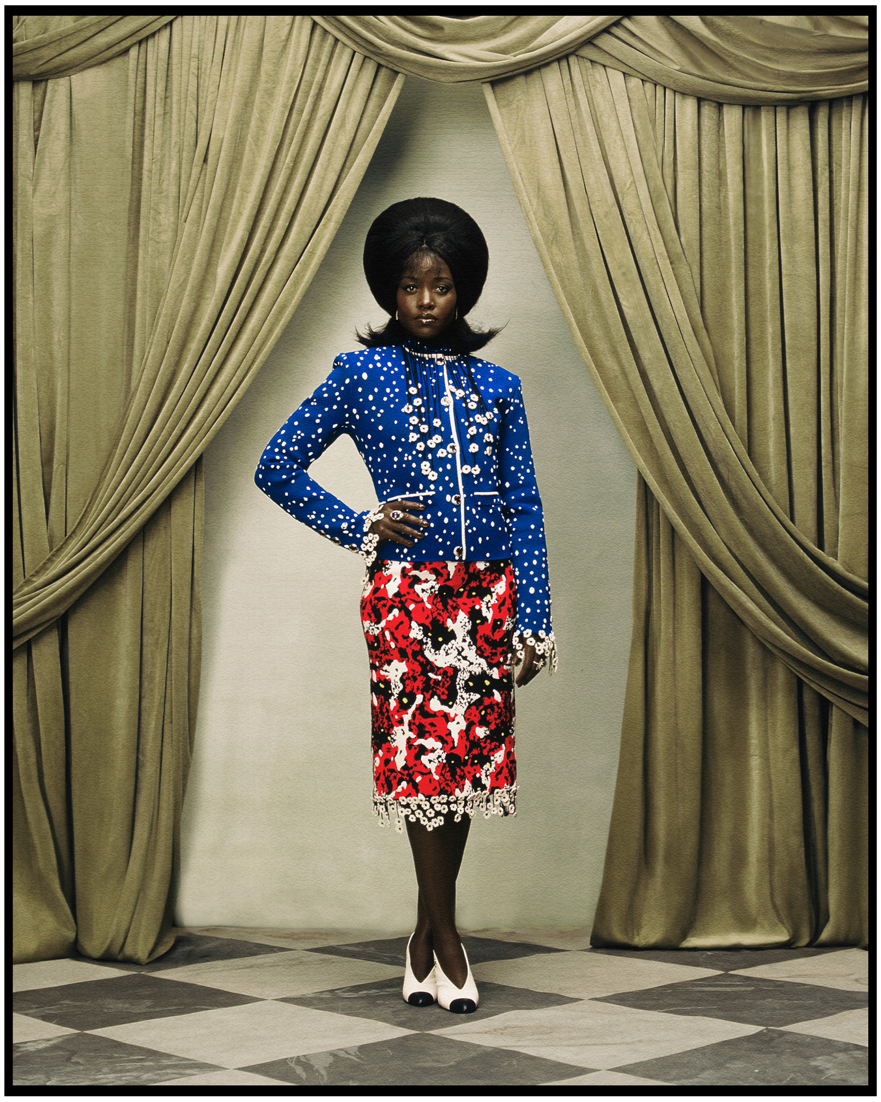 Lupita Nyong'o photographed by Kenny Germe&amp;#769;. She is standing in front of a velvet curtain wearing a Chanel blue jacket with white dots and a red pencil skirt.