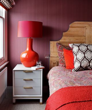 An example of bedroom lighting ideas showing a bedroom with red walls and a red table lamp