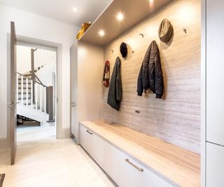 modern boot room with simple white doors, a light timber seat and seamless back panel with hooks and coats