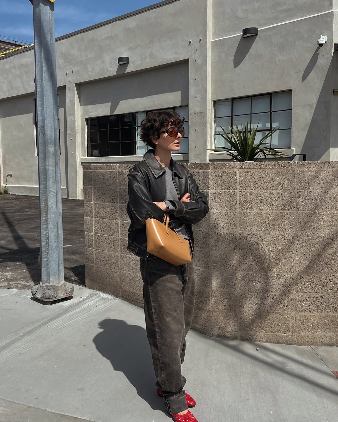 An influencer wearing a brown leather jacket, brown jeans and red ballet flats