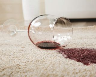 A wine glass containing red wine spilled on light cream carpet floor decor