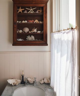 classic bathroom with shiplap half walls, cafe style curtain, marble topped basin, vintage wall cabinet