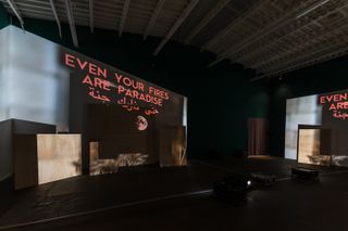A dark studio area with "EVEN YOUR FIRES ARE PARADISE" written in orange text on the left and right side.
