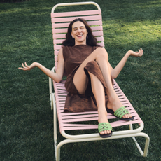 Model on a light pink sun lounger wearing a brown dress and mint green sandals sold at Tory Burch