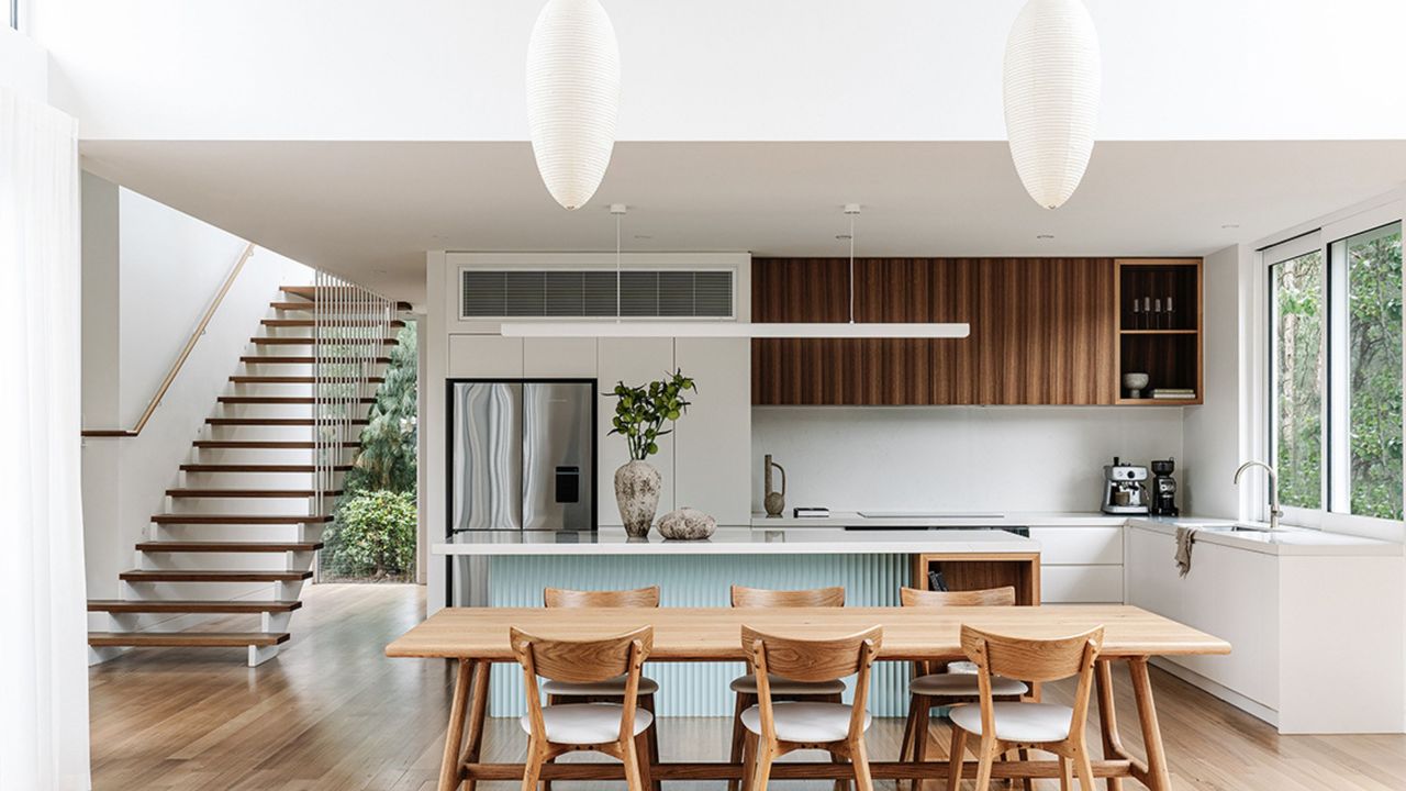 A tidy kitchen and dining area with white cabinets and wood upper cabinets on one side, with stairs to the side