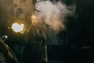 a woman (Sofia Vergara as Griselda) is seen firing a gun mid-shot, with a flash of light around the barrel and a puff of smoke near her head