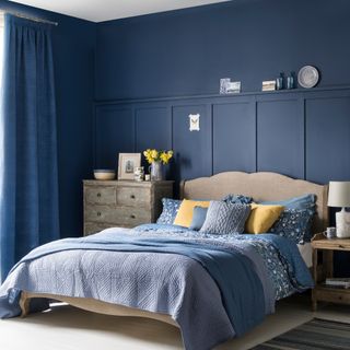 Blue bedroom with wall panelling and wooden furniture