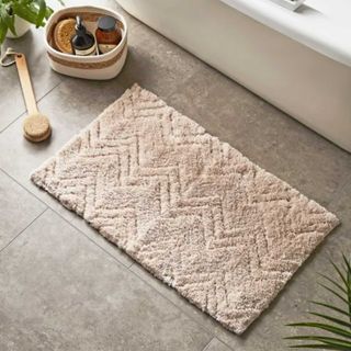 Textured beige bath mat on the floor beside a freestanding bath
