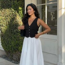 Woman wears black waistcoat and white midi skirt