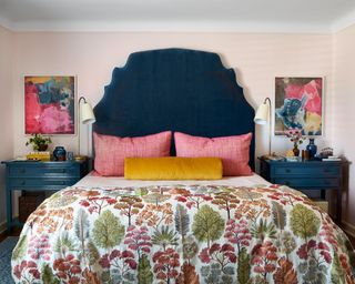 colorful bedroom with dark blue headboard and nightstands, light pink walls, pink and mustard pillows and patterned quilt