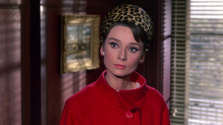 audrey hepburn in a red coat and leopard print hat in a still from charade