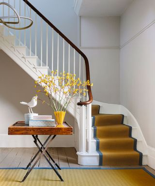 Colorful entryway with yellow rug and stair runner, wooden table decorated with books and flowers, sculptural hanging pendant light
