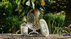 a diptyque candle with a vase of flowers on wood outside