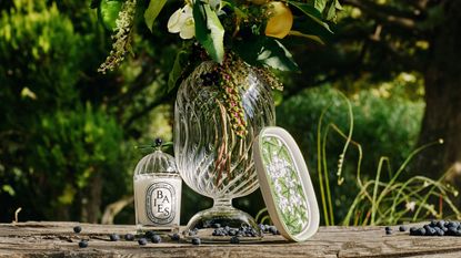a diptyque candle with a vase of flowers on wood outside