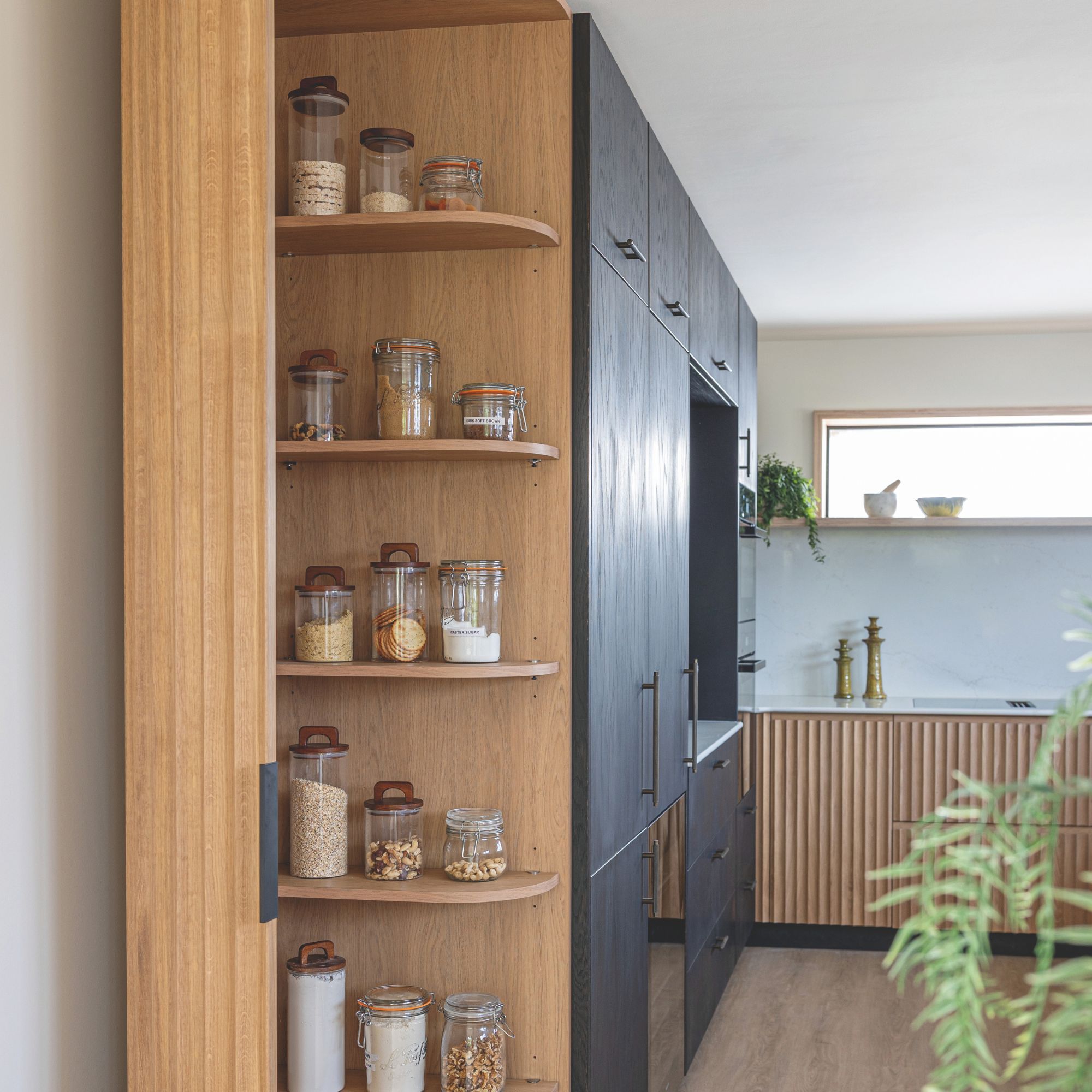 Black wood kitchen with natural accents, hidden pantry in floor to ceiling unit