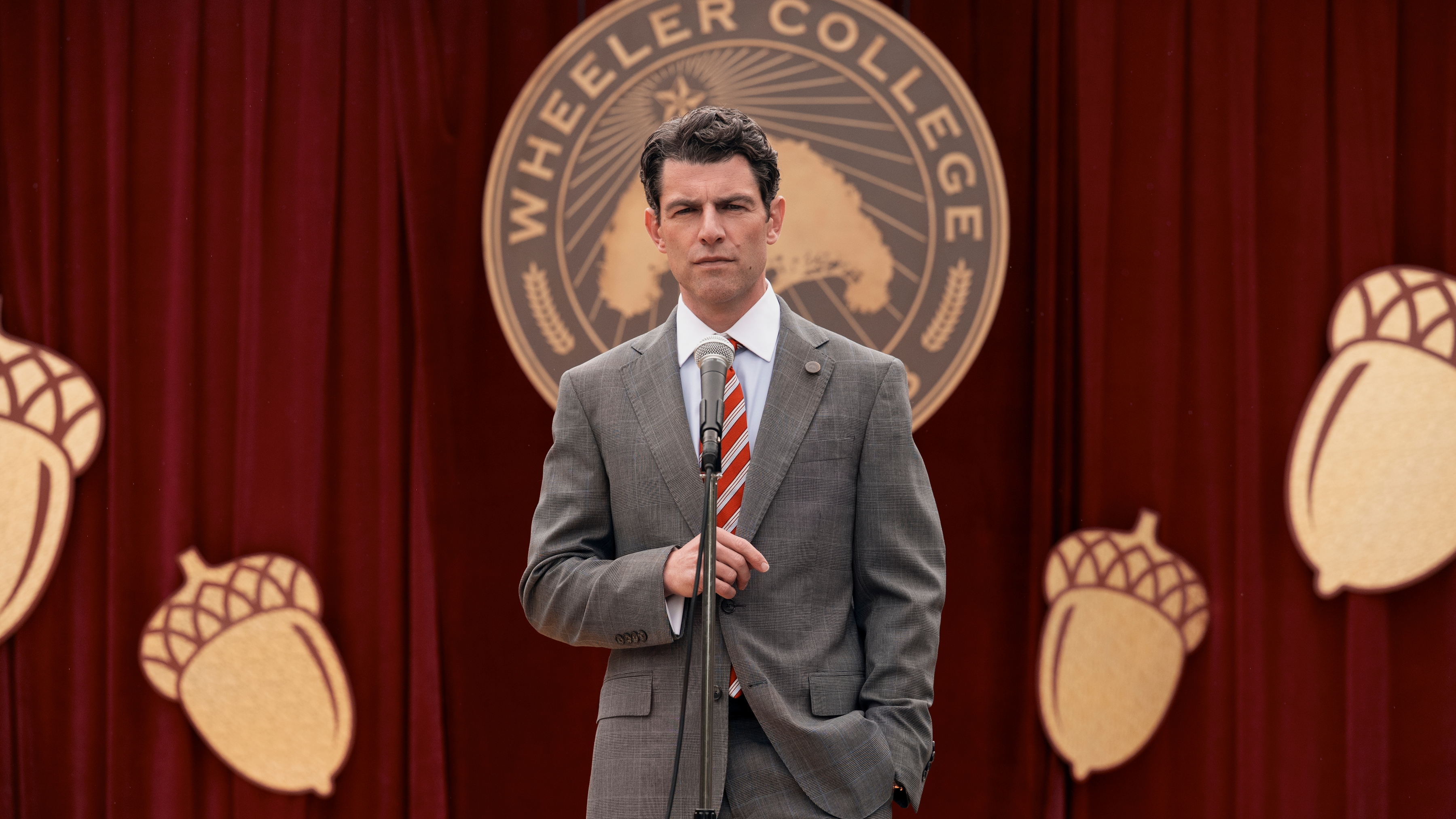 Berenger (Max Greenfield) stands in front of the Wheeler College logo in a scene from "A Man on the Inside" season 2