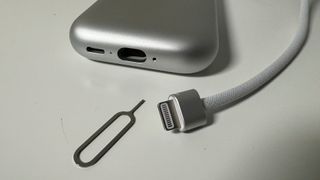 Le connecteur de la batterie de l'Apple Vision Pro, à côté de la batterie elle-même et d'un outil pour retirer la carte SIM.