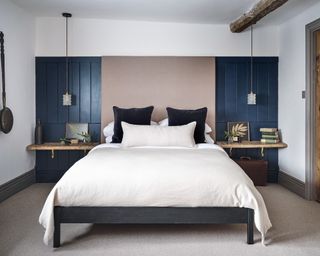 bedroom with navy blue panelling, glass pendant lights and gray bed with neutral bedlinen