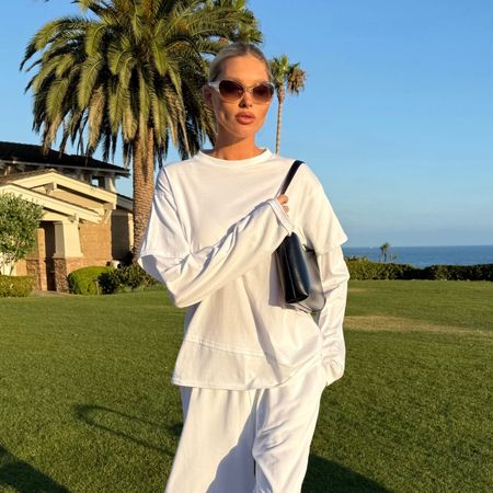 Model @hoskelsa wears longline shorts with a white long-sleeve top and black flip-flops.