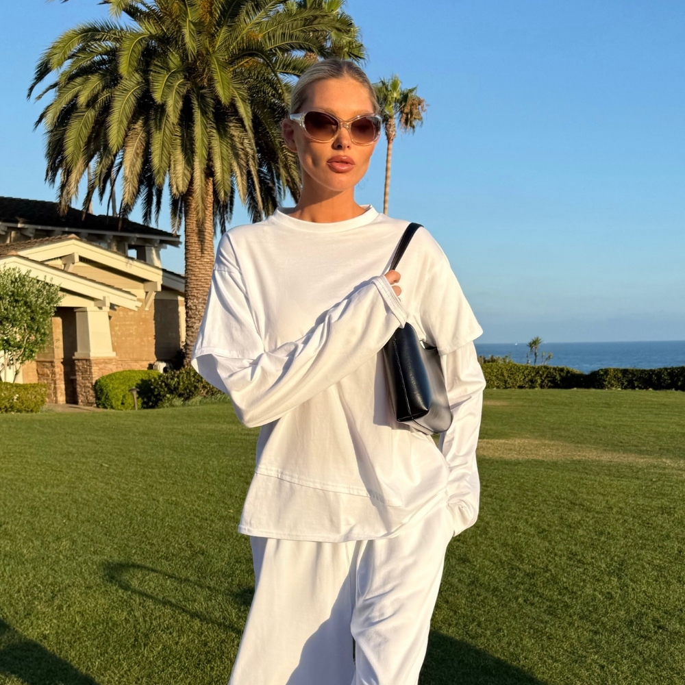 Model @hoskelsa wears longline shorts with a white long-sleeve top and black flip-flops.