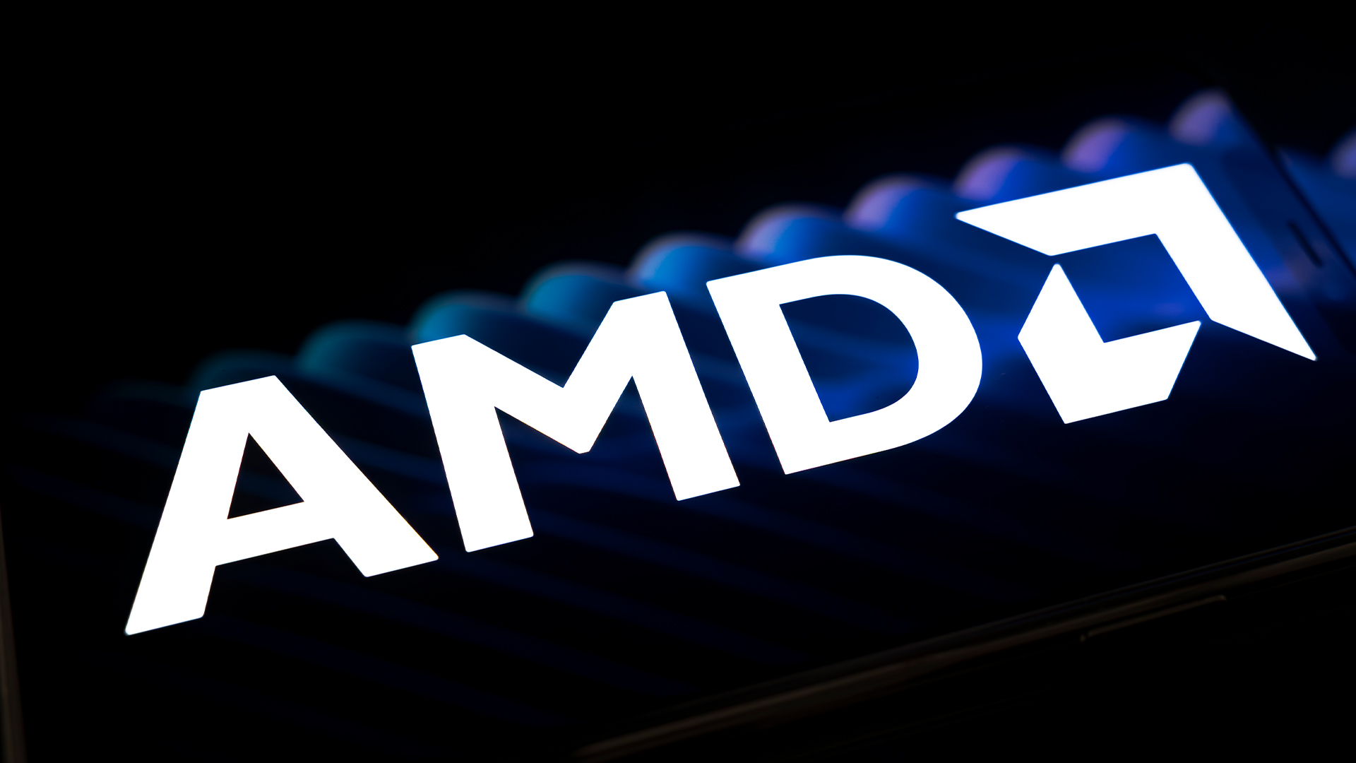AMD logo and branding pictured on a dark reflective surface with faint blue lighting in background.
