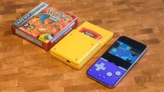 Box of Pokémon FireRed on Game Boy Advance next to a yellow Analogue Pocket next to an iPhone 15 Pro Max running Delta Game Emulator with Goodboy Galaxy demo