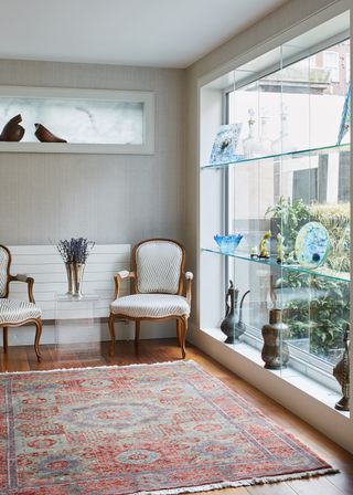 Living room with large window with glass shelves, rug and armchairs
