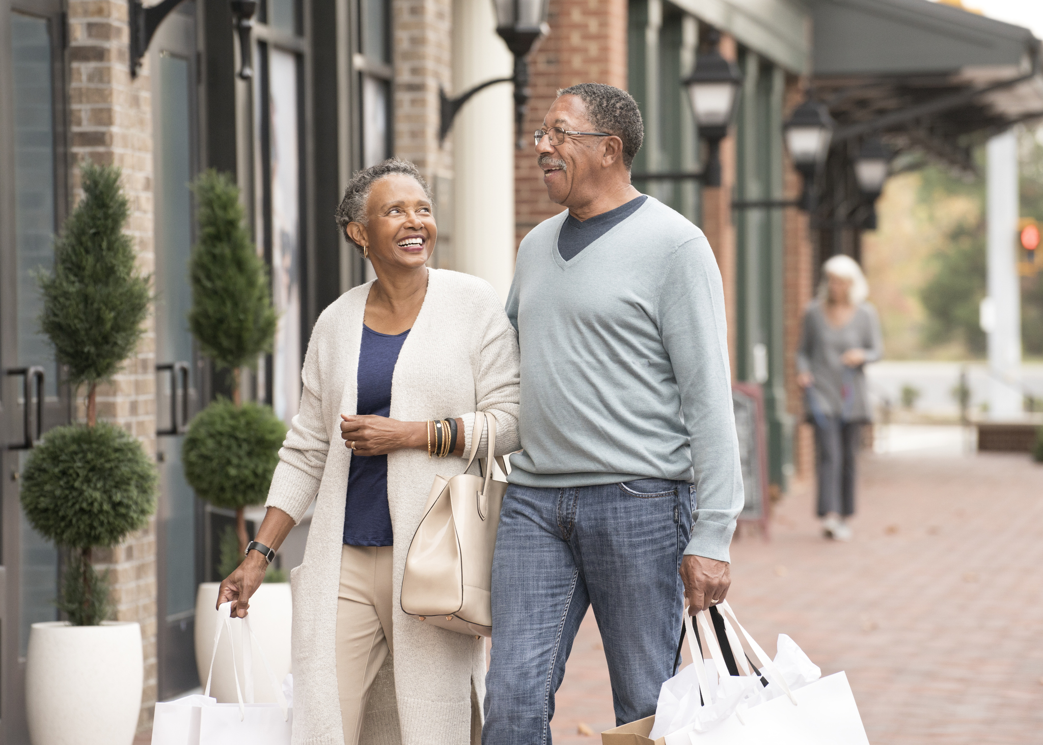 A mature, affluent couple walks down the street with shopping bags.