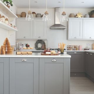 A kitchen with grey and white cabinets decorated for Christmas with a wreath and tabletop paper trees