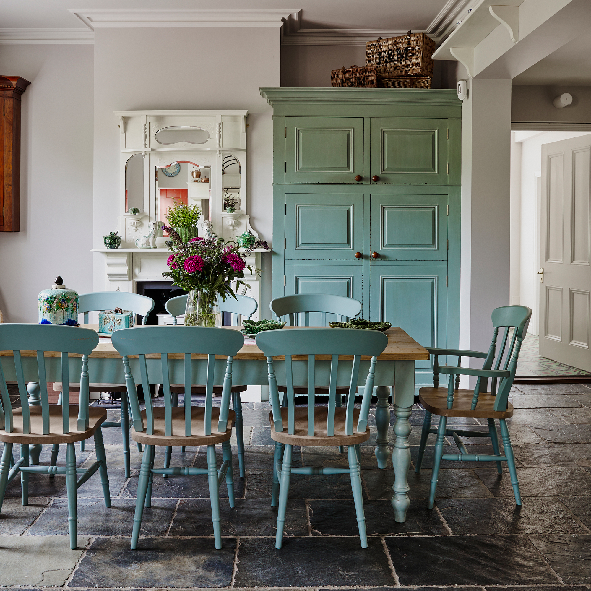 country dining room with stone floor tiles, light blue painted farmhouse table and chairs and laundry cabinet