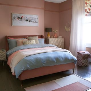bedroom with pink wall wooden flooring and pink bed with blue cushions